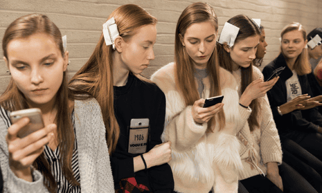 Models backstage at a fashion show, staring at their phones