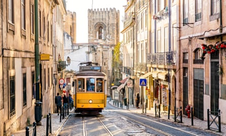 Street in Lisbon’s old town with yellow tram and Lisbon Cathedral in the background. Lisbon, Portugal