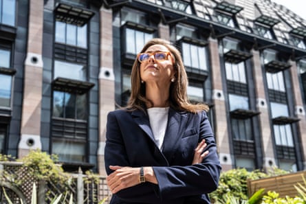 Lauren Edwards stands in front of a tall modern building, looking upwards. She has long, straight dark hair and wears glasses, and a dark navy jacket over a white top.
