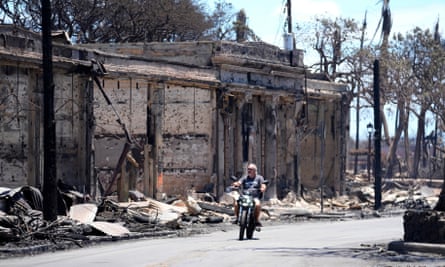 A man rides his motorcycle amid damage caused by wildfire in Lahaina.