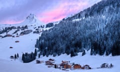 Snowy mountains with pink evening light behind them, and little Alpine buildings nestled at the bottom.