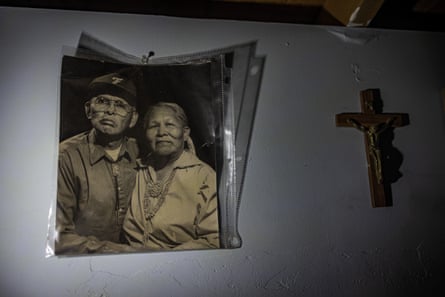 A yellowed, black-and-white photo of an older Indigenous couple, holding each other and looking amiably at the camera, beside a small cross on the wall.