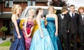 A group of four girls in colourful evening (school prom) dresses and three boys in dinner and evening suits standing in front of a yellow campervan and house in background