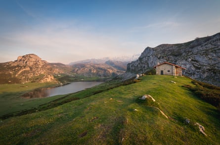 A stone hut by a lake with mountains in the background