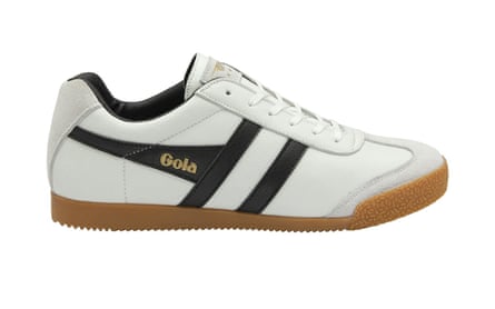 The side view of a white Gola trainer. It has the Gola name in gold across a black stripe. There are two further black stripes. It is on a white background.