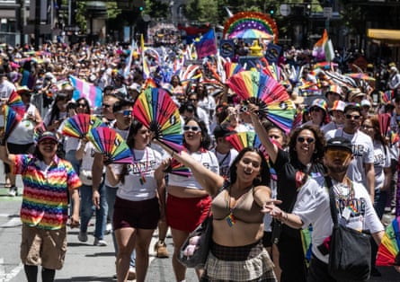people wearing rainbow clothes and waving rainbow-colored fans walk in a parade