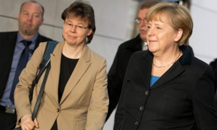 Baumann in beige jacket beside Merkel in black