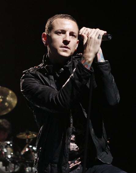 Chester Bennington wears a black jacket and holds a microphone as he performs on stage