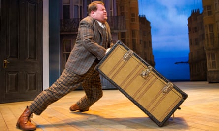 Man pushing a large suitcase across a stage.