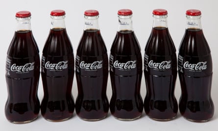 Une rangée de six bouteilles de Coca-Cola en verre avec couvercles rouges