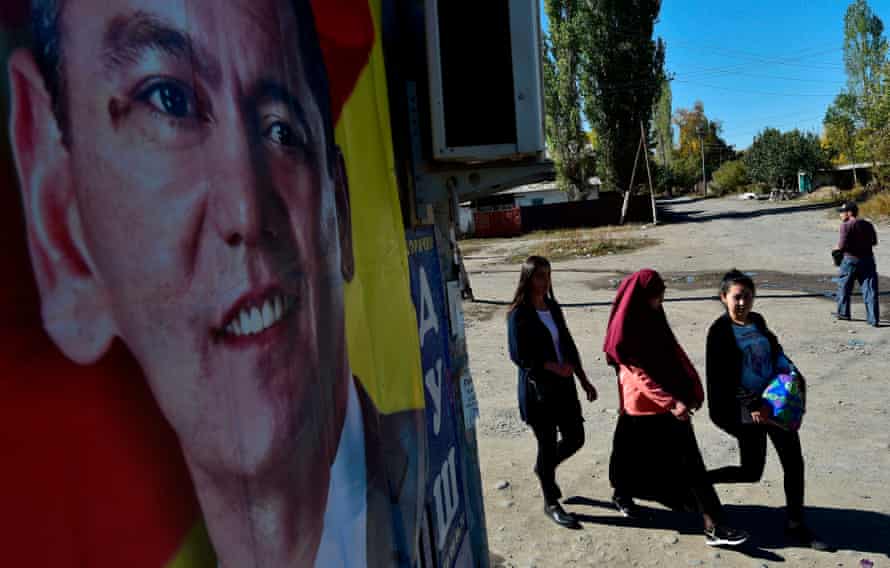 Women walk past an election campaign poster of Kyrgyz opposition presidential candidate Omurbek Babanov in the outskirts of Bishkek.
