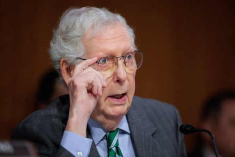 a man in a suit speaks while adjusting his glasses with his hands