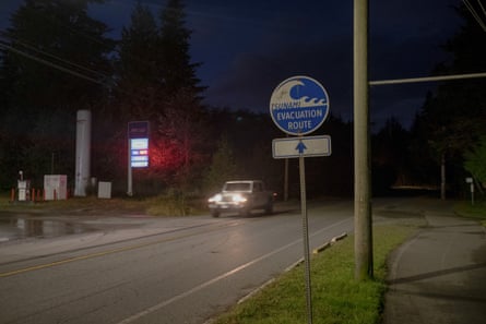 A sign at the side of a road at night reads ‘tsunami evacuation route’. A car can be seen in the background.