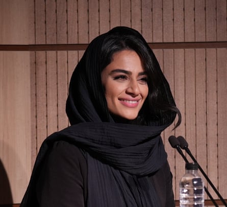 A smiling Persian woman wearing a black headscarf at a podium