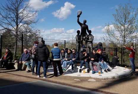 West Ham fans sit around the statue of Martin Peters, Bobby Moore and Geoff Hurst that was erected outside the London Stadium to remember the Hammers’ 1965 victory in the European Cup Winners Cup