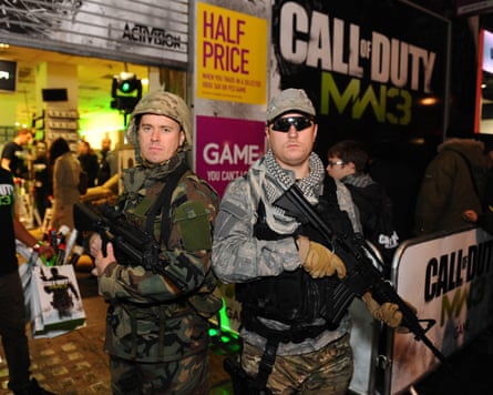 Two men dressed as soldiers carrying large guns stand outside a games shop.
