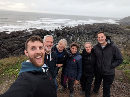 Six people in walking gear with a grey sea and rocky shoreline behind them