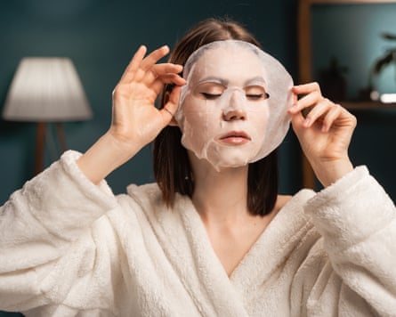 Woman in a dressing gown with a cloth moisturising mask on her face in her bedroom