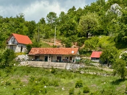 Some simple buildings with terracotta tiled roofs, among trees on a green hillside