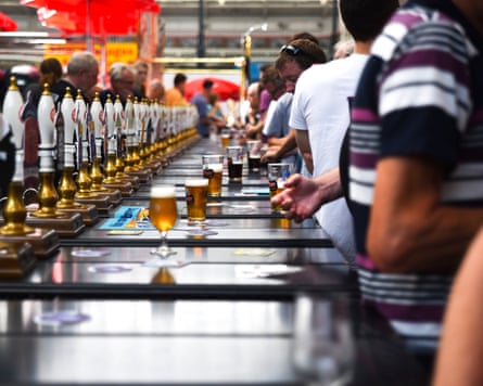 View along a long bar of pumps on one side and customers on the other, with pints of beer along the bar