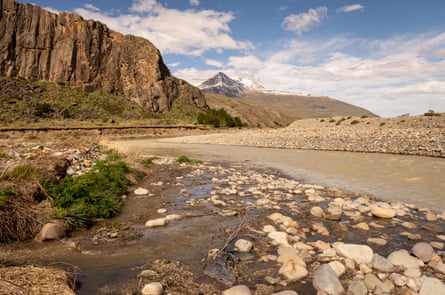 A river light brown in colour with darker brown water along its rocky banks with mountains in the background