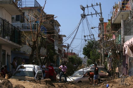People work to free cars stuck in the mud in the aftermath of Hurricane Otis in the Progreso district of Acapulco.