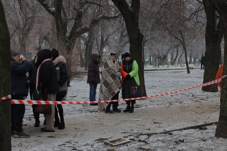 People standing in a snowy park, one of the wrapped in a blanket