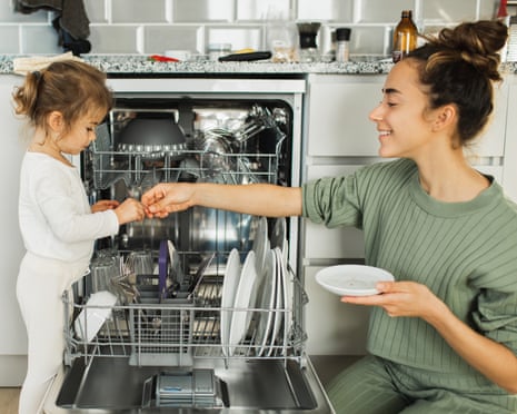 Little girl helping her mother and loading the dishwasher at home.