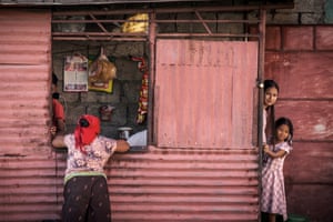 Two children peer out from a pink corrugated iron facade