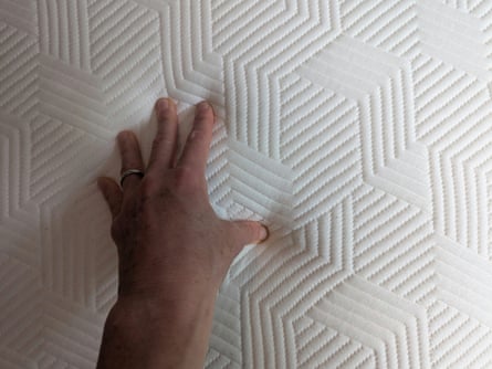 A hand squishes into a Panda Hybrid mattress in close up showing the art deco detail pattern in the mattress cover.