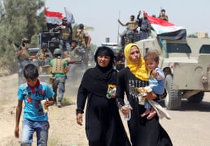 Iraqi families walk along the road past pro-government forces after fleeing the city