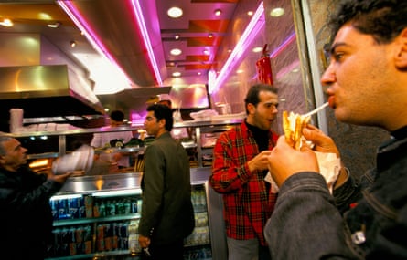 Men eat sandwiches in a neon-lit sandwich bar
