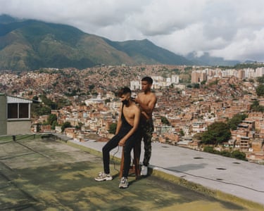Petare, 2021 . One man cuts a young man's hair, on the roof of a building overlooking the city