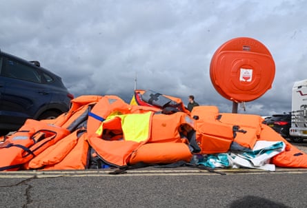 Pile of orange lifejackets on a grey concrete wall
