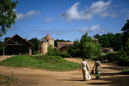 Two women in 13th-century dress approach the turreted walls of Chateau Guedelon