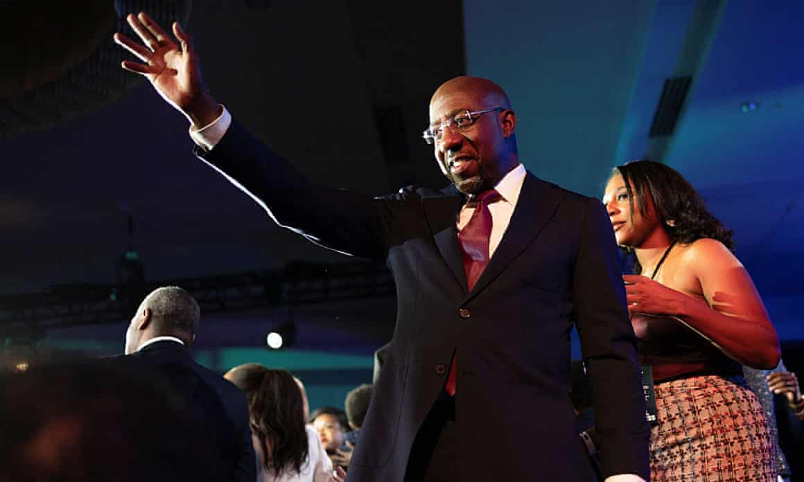 Raphael Warnock in a suit gesturing with one hand.