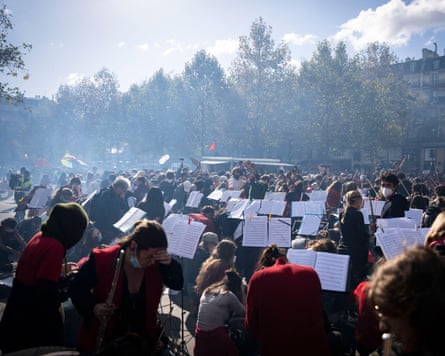 Musicians with sheet music on their stands perform in Place de la République, as some grab masks to shield them from the smoke.