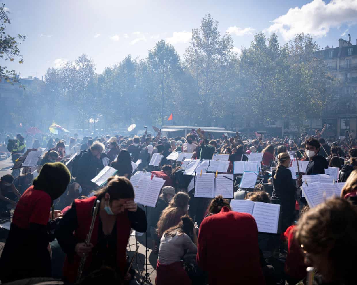 Musicians with sheet music on their stands perform in Place de la République, as some grab masks to shield them from the smoke.