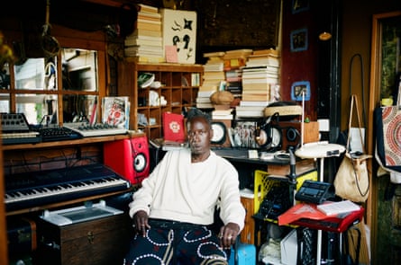 Saul Williams dressed in a white top in a cluttered room with a piano