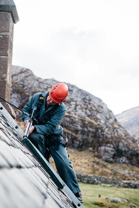 Robbie, a bothy volunteer, in hard hat and overalls, repairs a bothy roof.