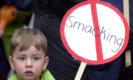 A child holds a placard showing the word 'smacking' inside a red prohibition ring.