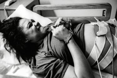 Black and white photograph of a woman handcuffed in a bed with tubes and straps taped to her stomach