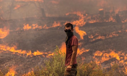 Un hombre está listo para combatir las llamas que engullen la ladera de una colina el 27 de julio en Apollana, en la isla de Rodas, Grecia.