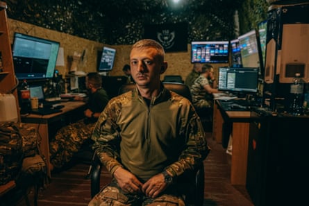 Denys Bryzhatyi sits in a chair with colleagues in front of screens behind him