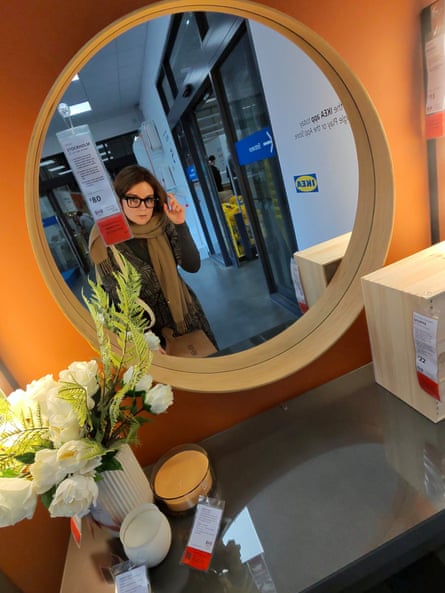 A woman in heavy-framed glasses looking into a mirror in an Ikea store
