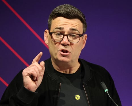 Burnham in glasses and a black jacket gestures with his finger raised while speaking at a microphone