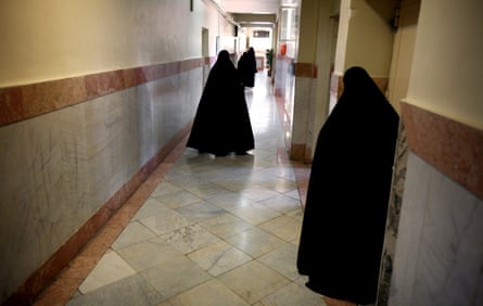 Women wearing black chadors walk in a narrow corridor