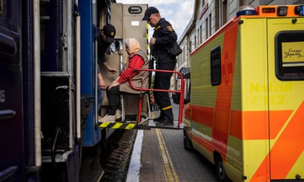 An elderly woman being lifted from an ambulance through a train carriage door