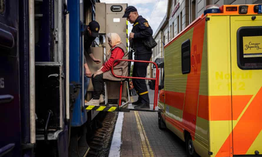 An elderly woman is lifted out of an ambulance through a train car door