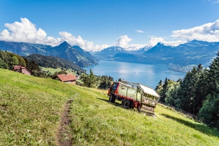 An agricultural vehicle on an alpine meadow with a lake and snow-capped mountains in the background